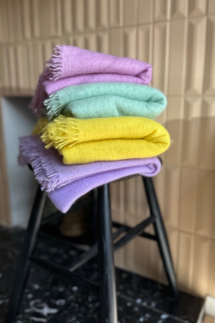Eighty scarf folded in pile of various colours on stool