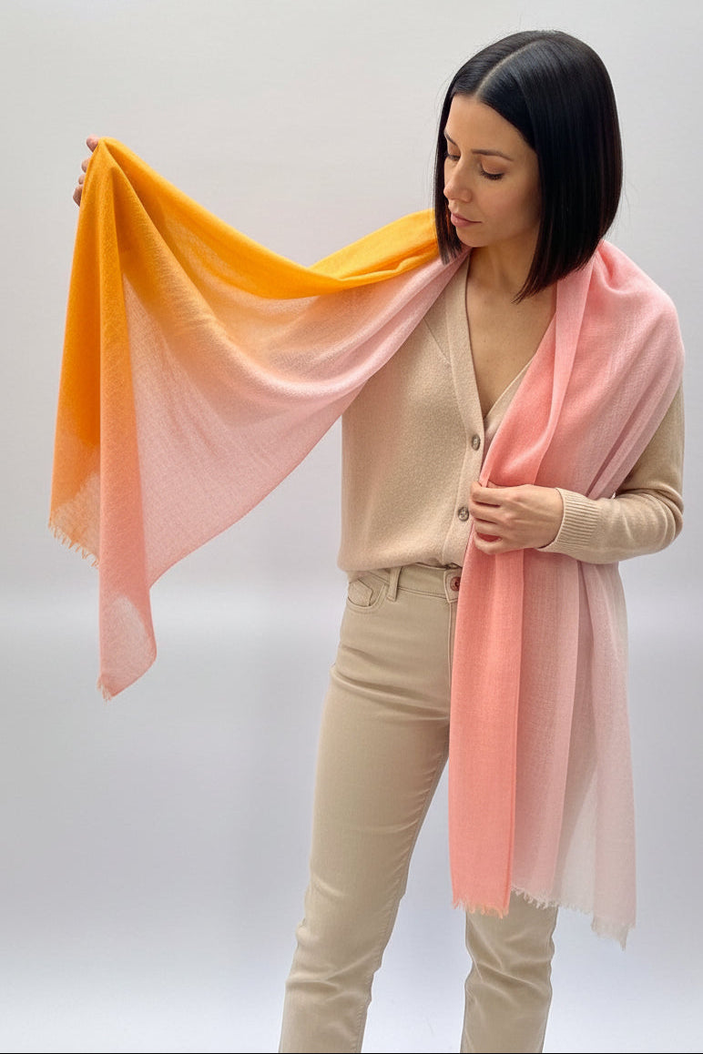 Woman holding a cashmere ombre pink orange scarf against a plain background