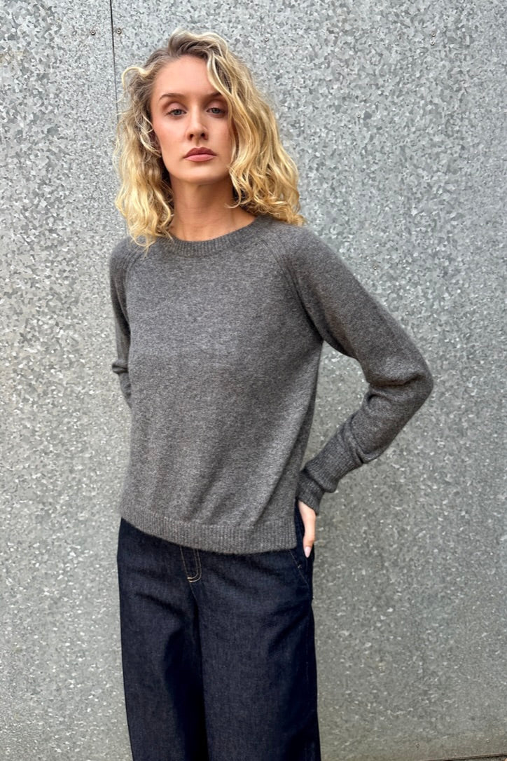 model wearing a gray grey hethna cashmere sweater and dark jeans against a textured wall.