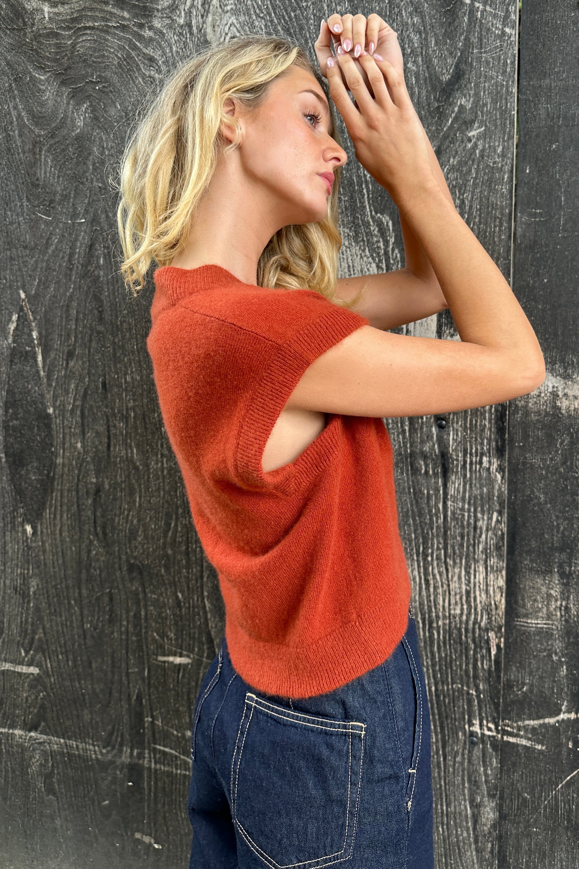 model wearing a rust-colored cashmere square neck knit tank top against a dark background side view