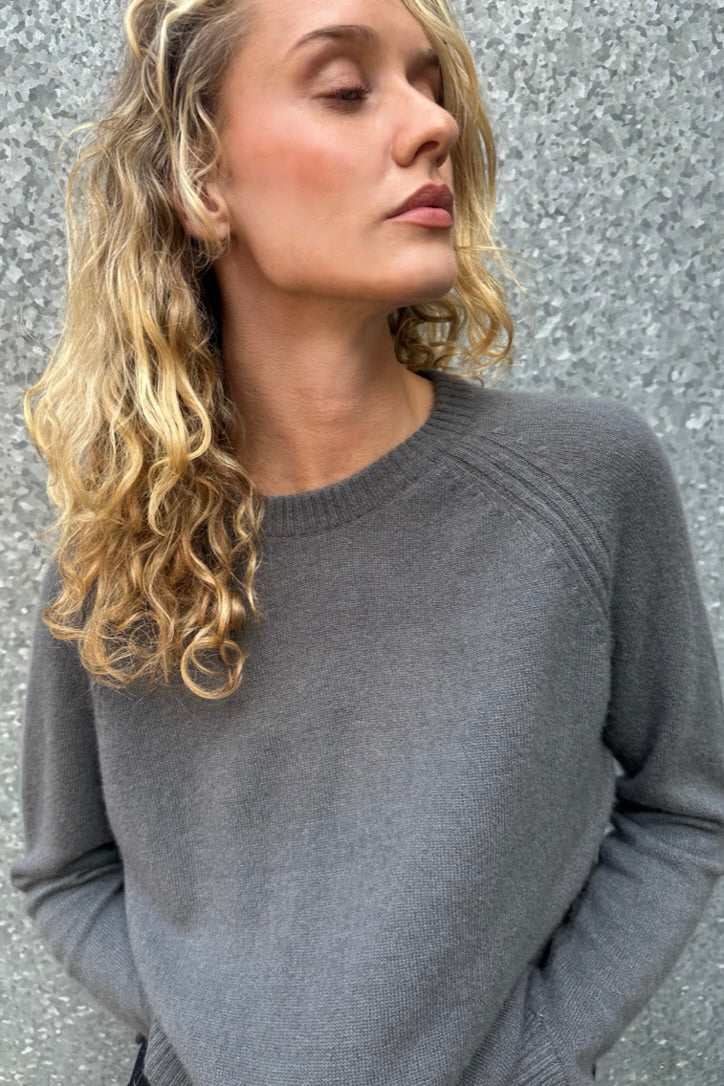 Woman wearing a gray sweater against a textured wall. close up