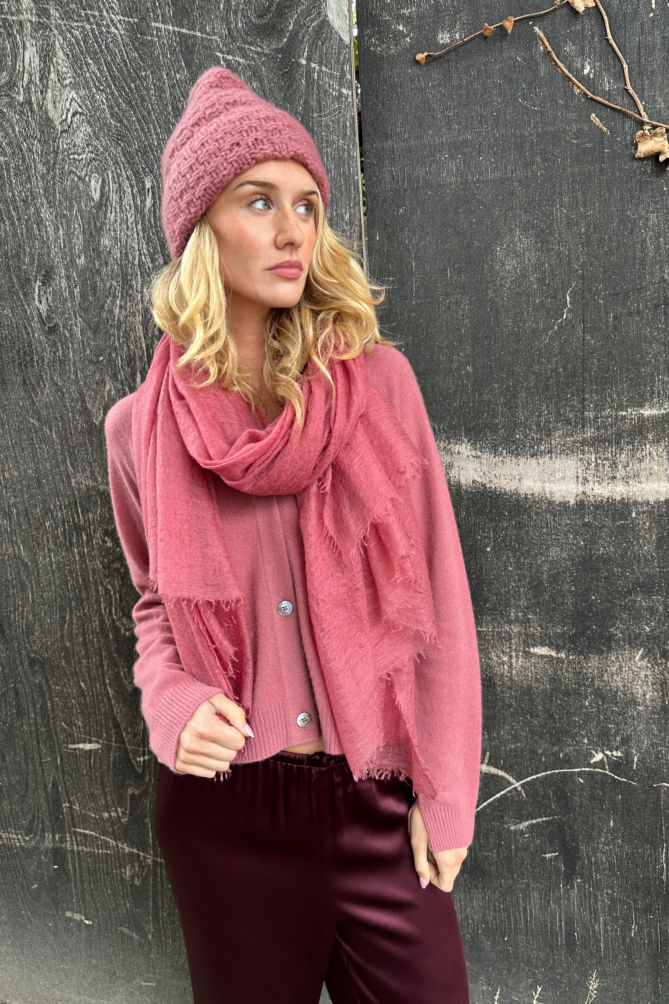 model wearing a pink knit hat and scarf against a textured blackmarmee khalo rose pink cashmere scarf