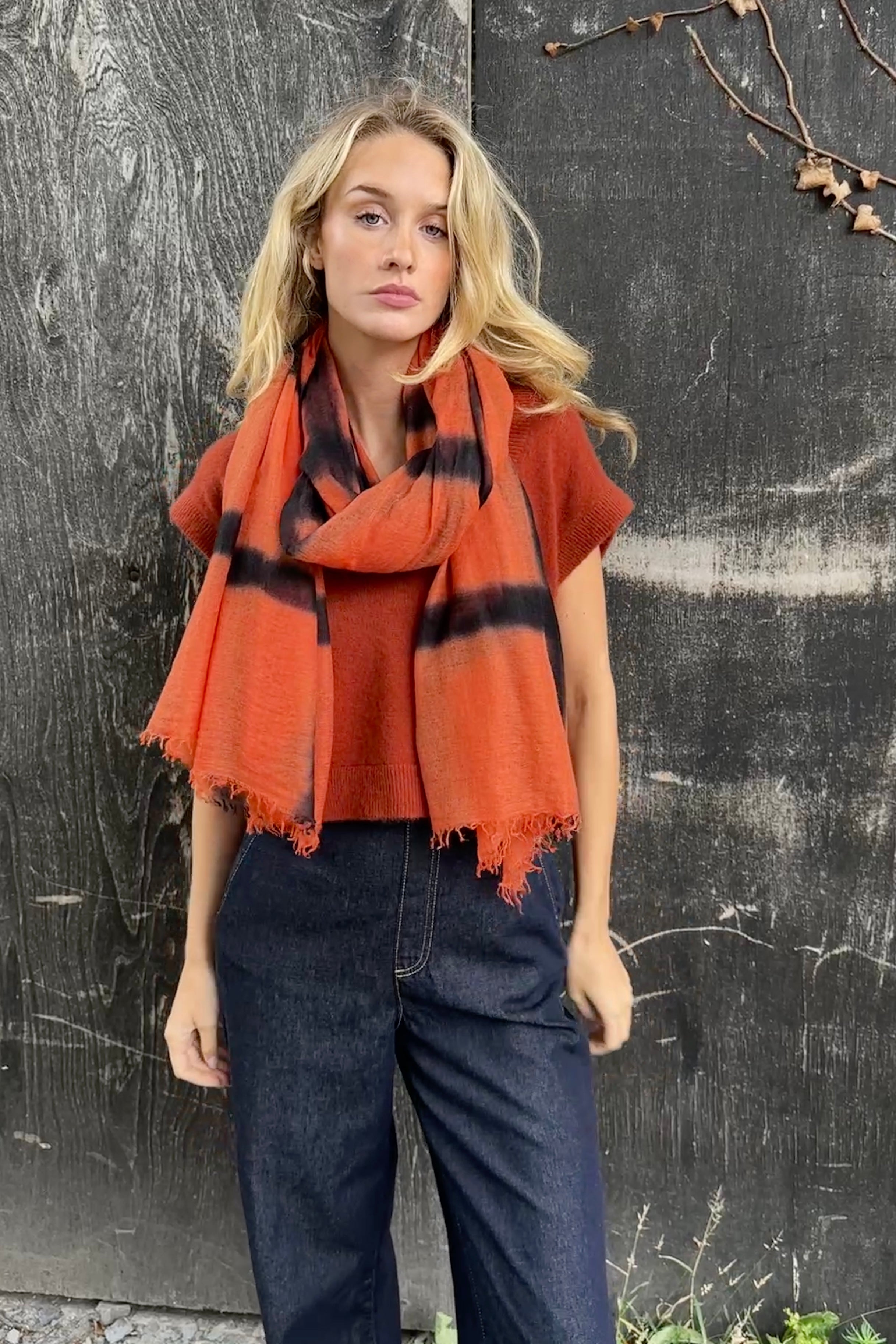 model wearing an orange and black stripe shibori tie dye scarf against a textured black background
