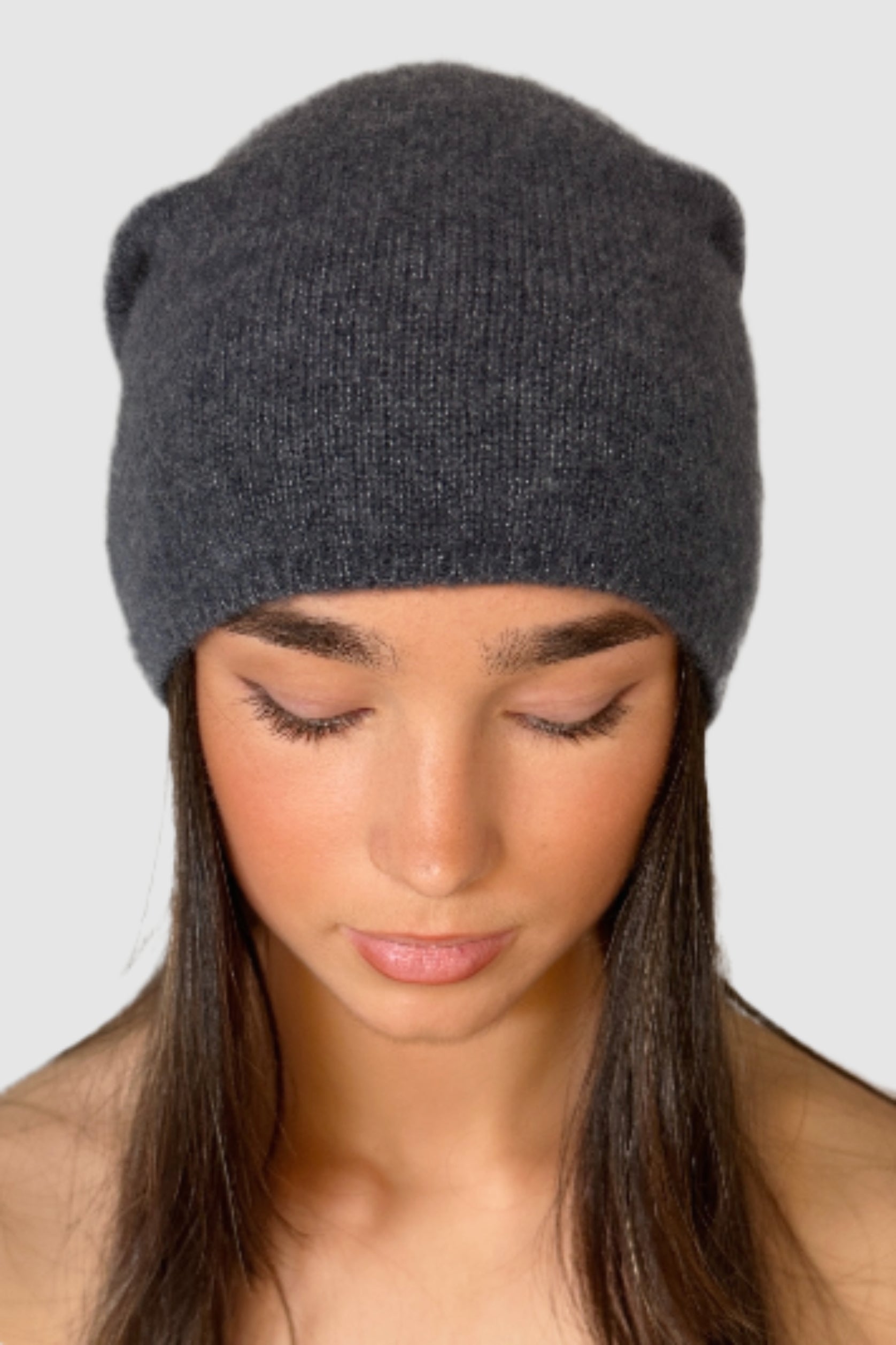 Woman wearing a dark blue gray knit beanie against a plain background