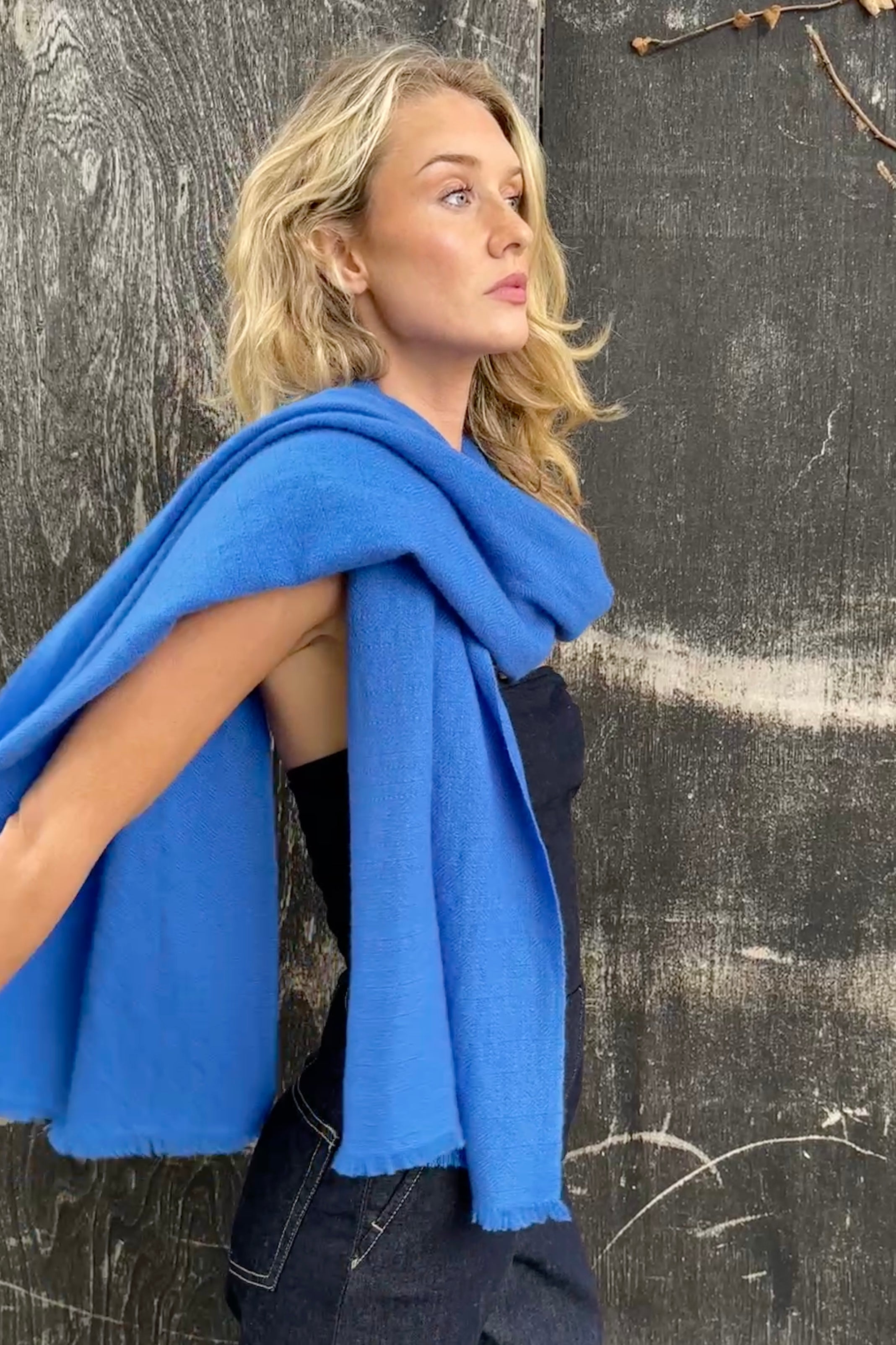 model wearing a blue kitty neon electric cashmere scarf against a textured dark wall side view