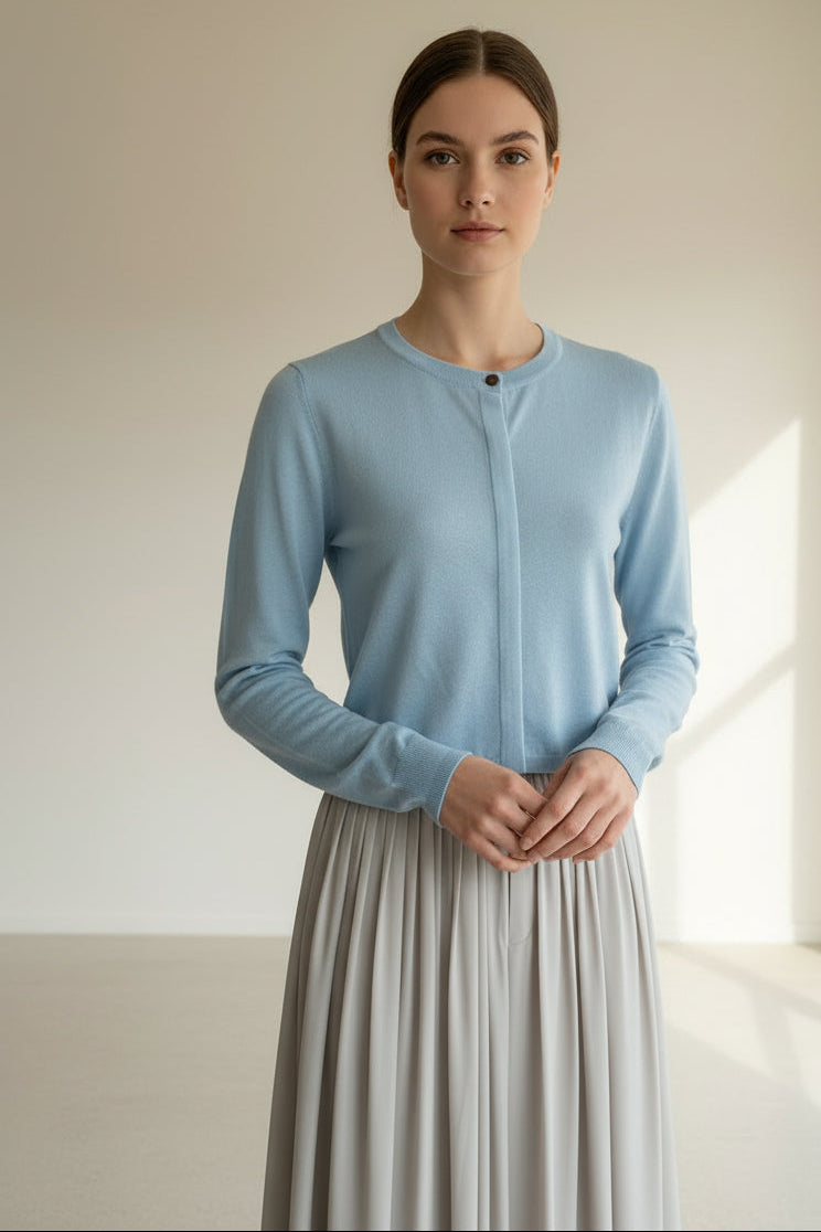 modelwearing a blue long-sleeve cardigan and gray skirt against a plain wall.