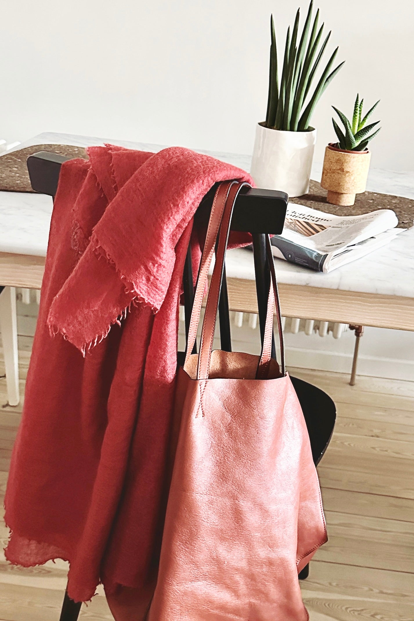 Pink marmee khalo scarf draped over a chair with a handbag underneath, on a wooden floor.