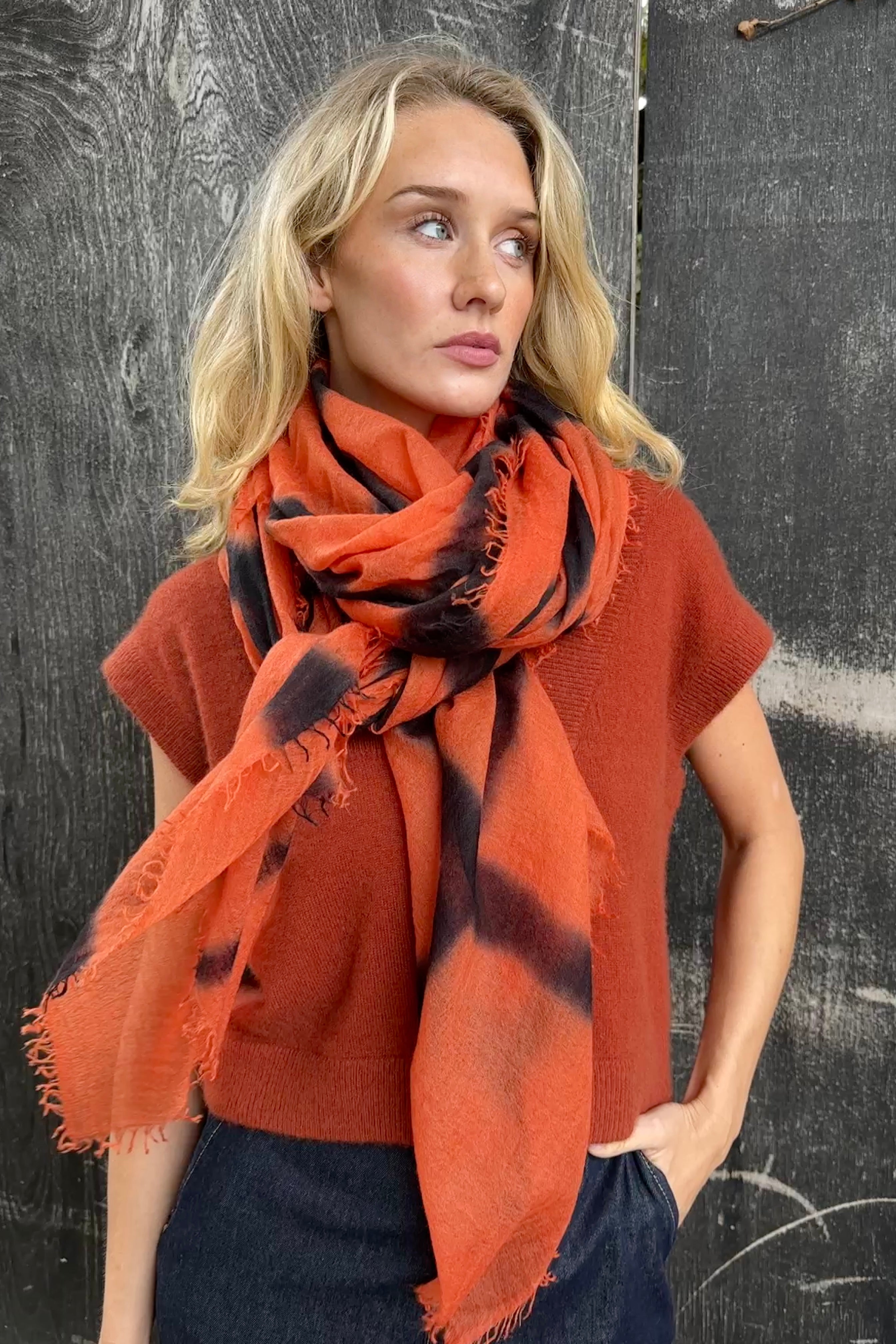 model wearing an orange and black stripe shibori tie dye scarf against a textured black background