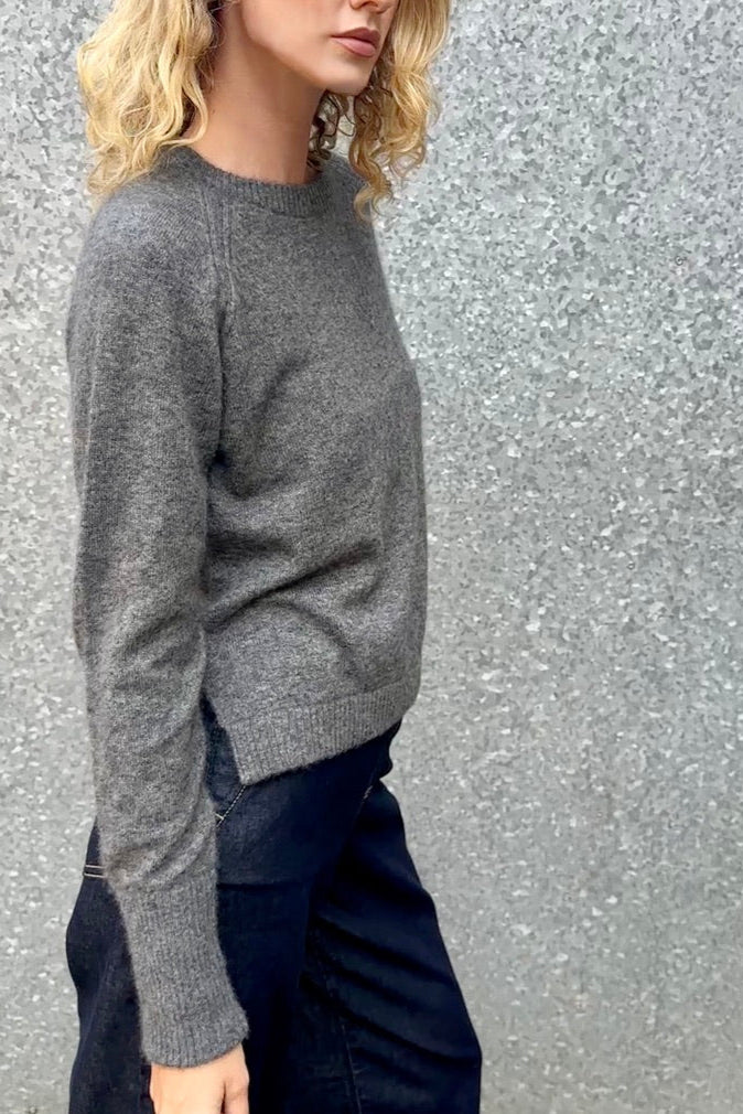 model wearing a gray grey hethna cashmere sweater and dark jeans against a textured wall. side view