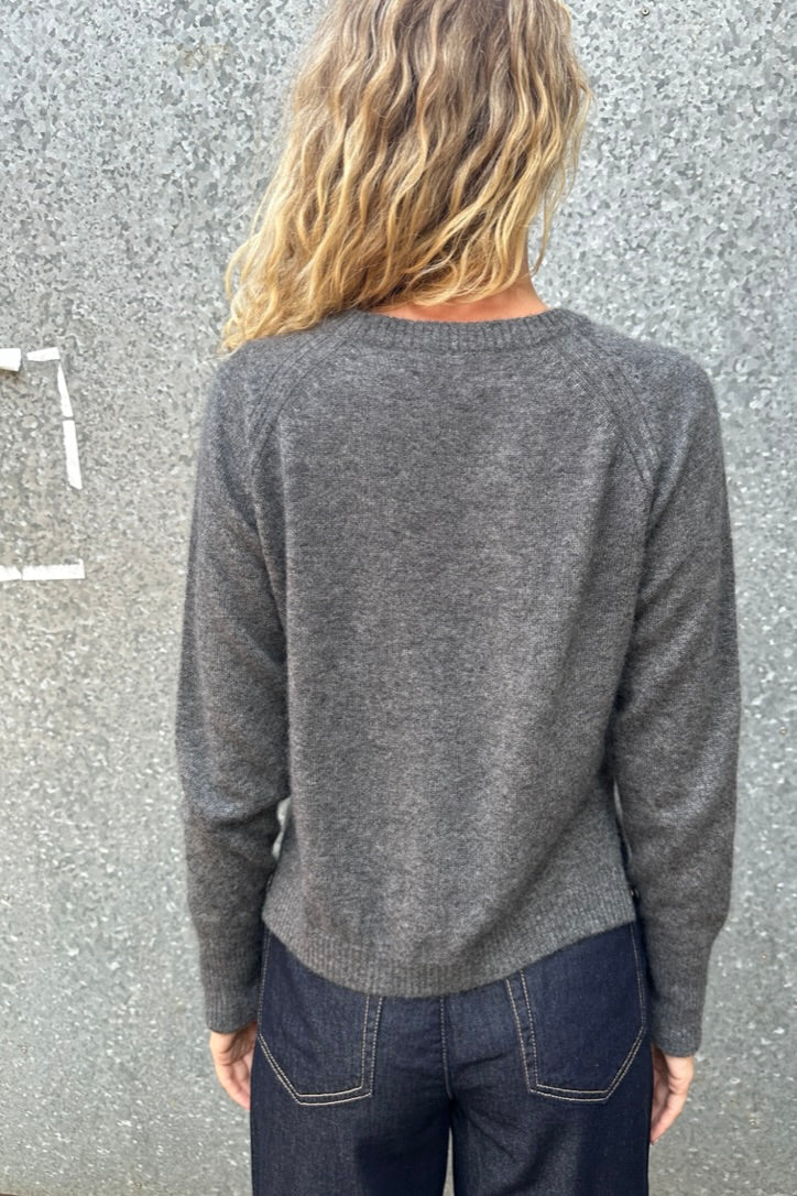 model wearing a gray grey hethna cashmere sweater and dark jeans against a textured wall. back view