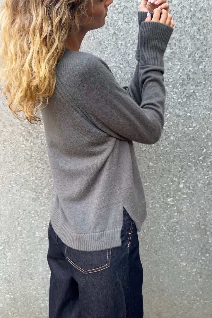 Person wearing a gray sweater and dark jeans against a textured wall.