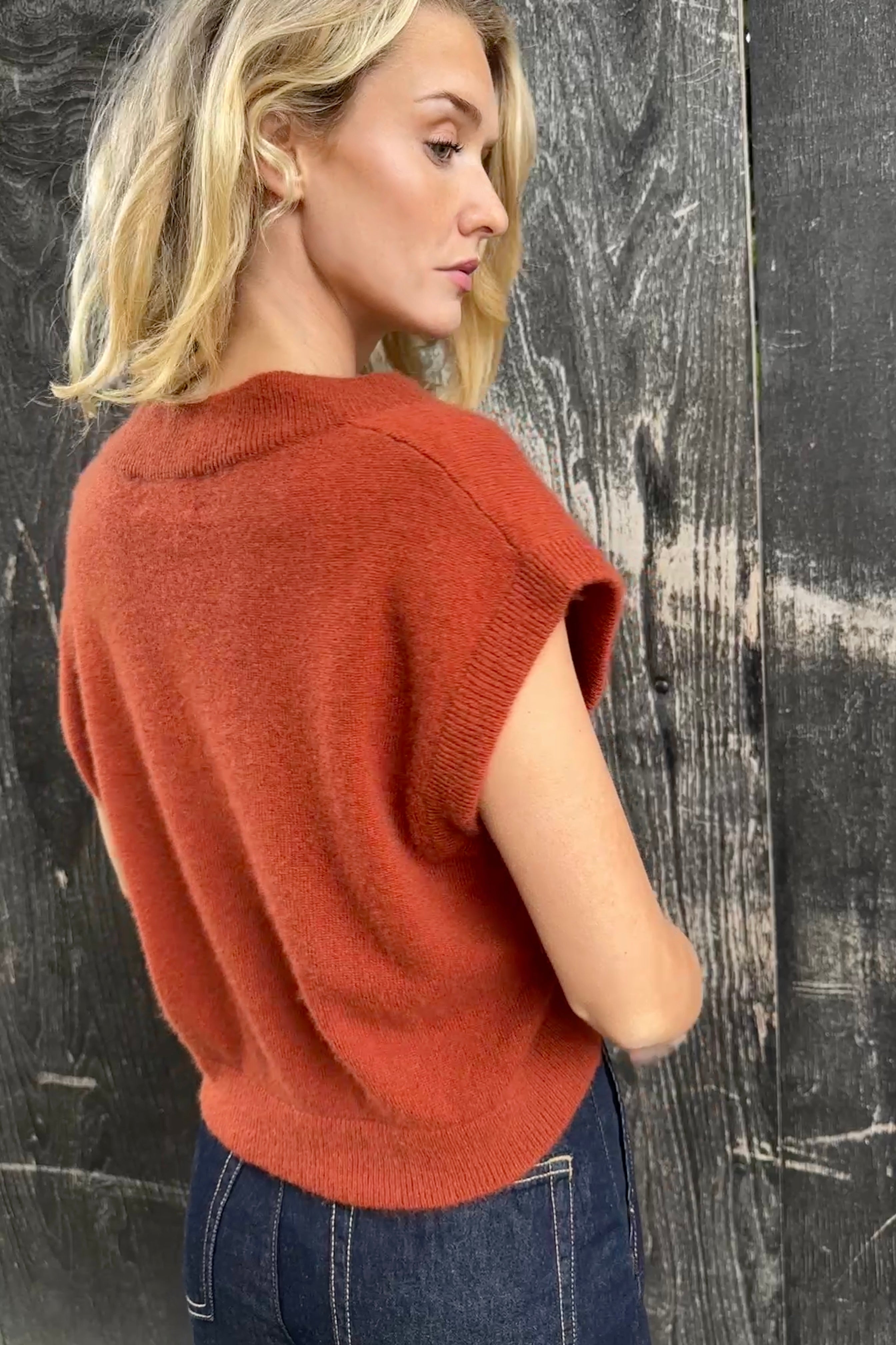 model wearing a rust-colored cashmere square neck knit tank top against a dark background back view