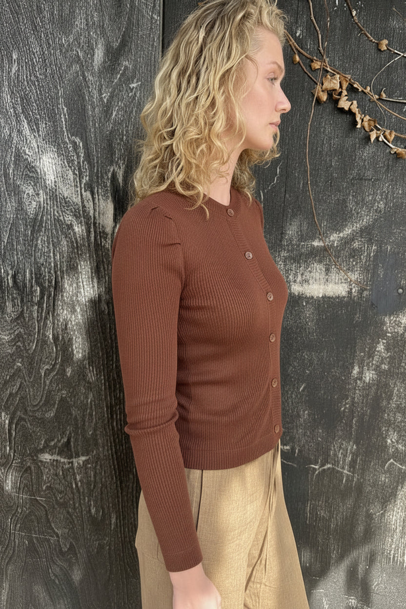 Woman in a brown cardigan and skirt standing against a textured dark wall.