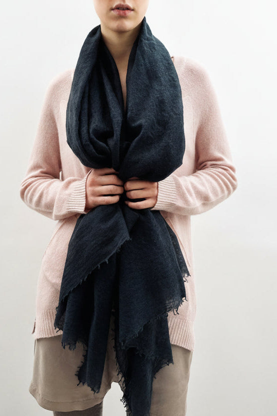 Person wearing a pink sweater and beige pants with a black scarf against a plain background