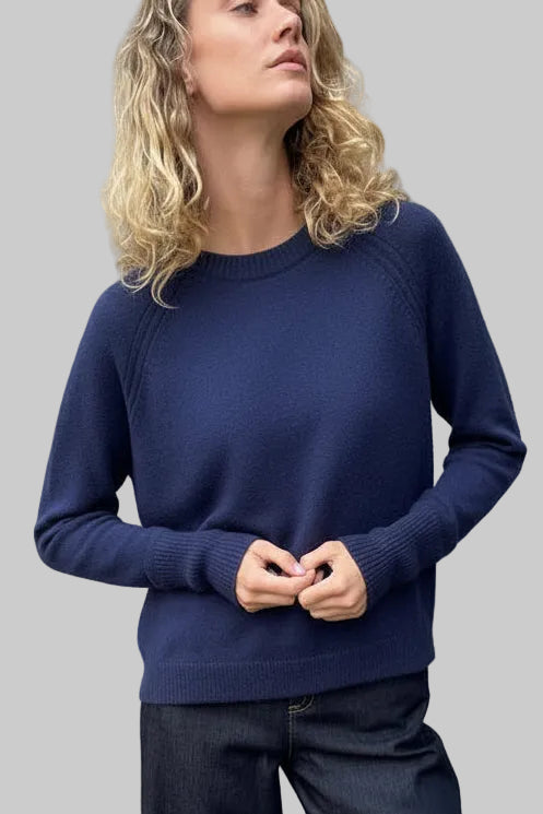 Person wearing a navy sweater and pants against a textured wall.