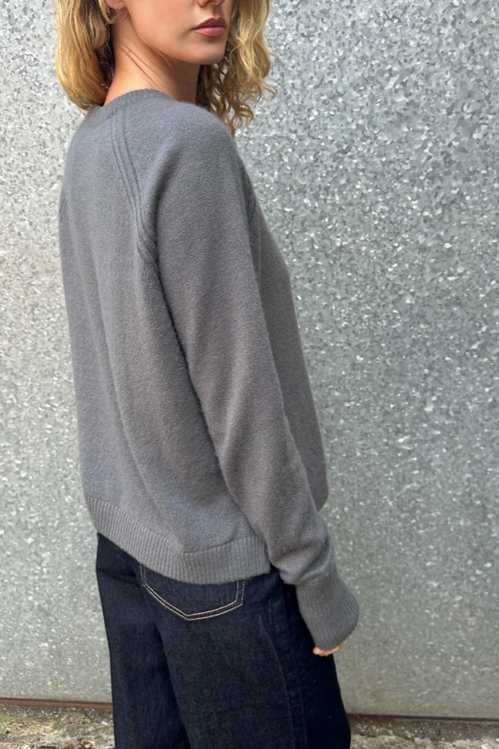 Person wearing a gray sweater against a textured wall.