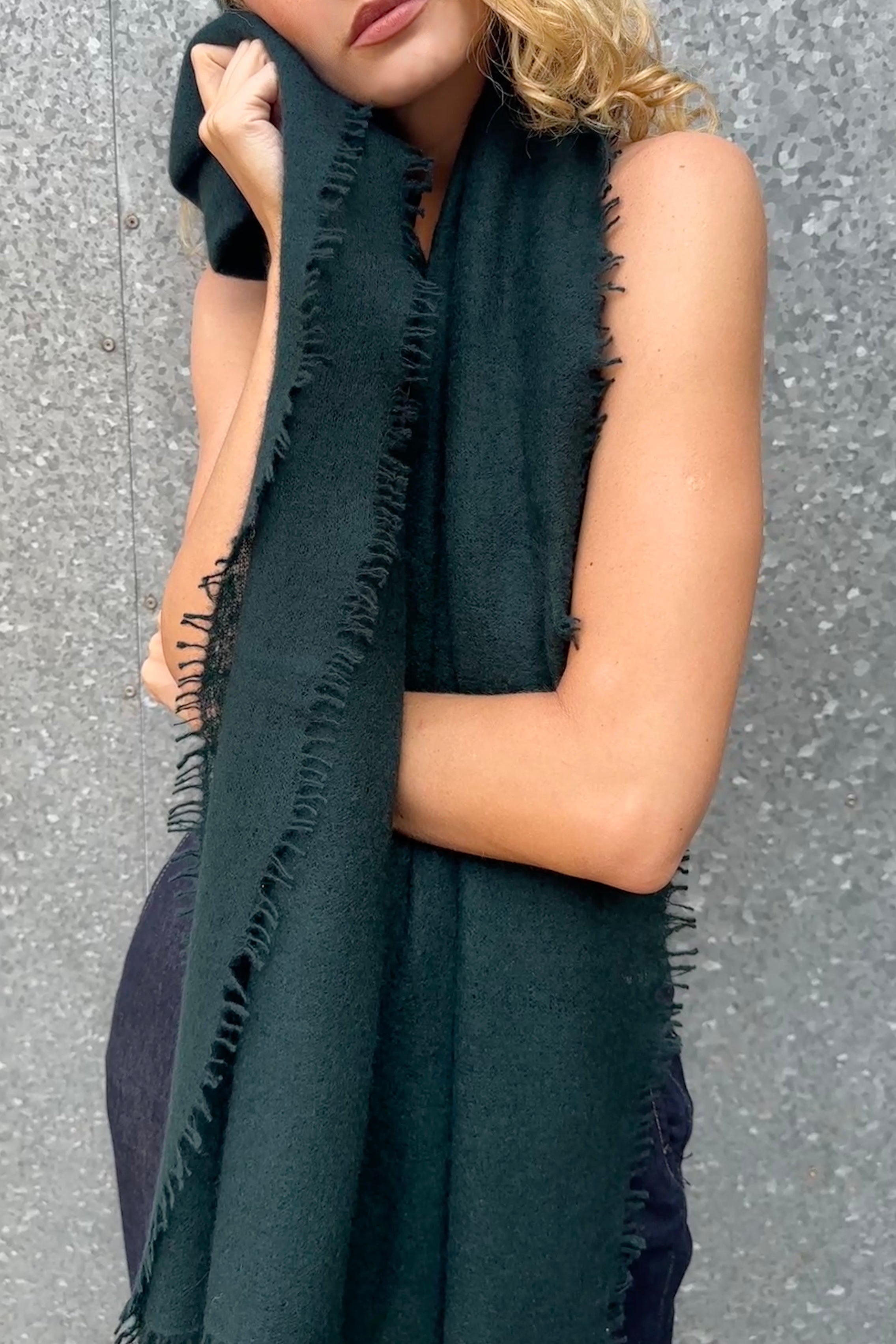 model wearing a dark green eighty cashmere scarf with fringe against a gray background