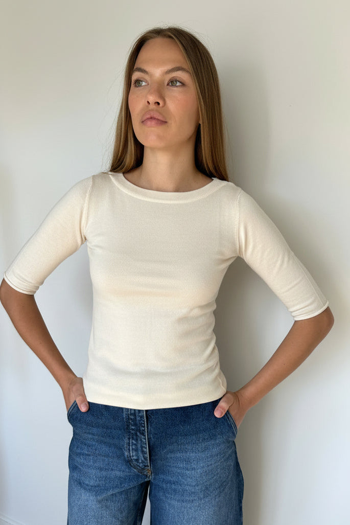A woman wearing a fitted ivory elbow length sleeve top and blue jeans, photographed from above against a plain white wall.