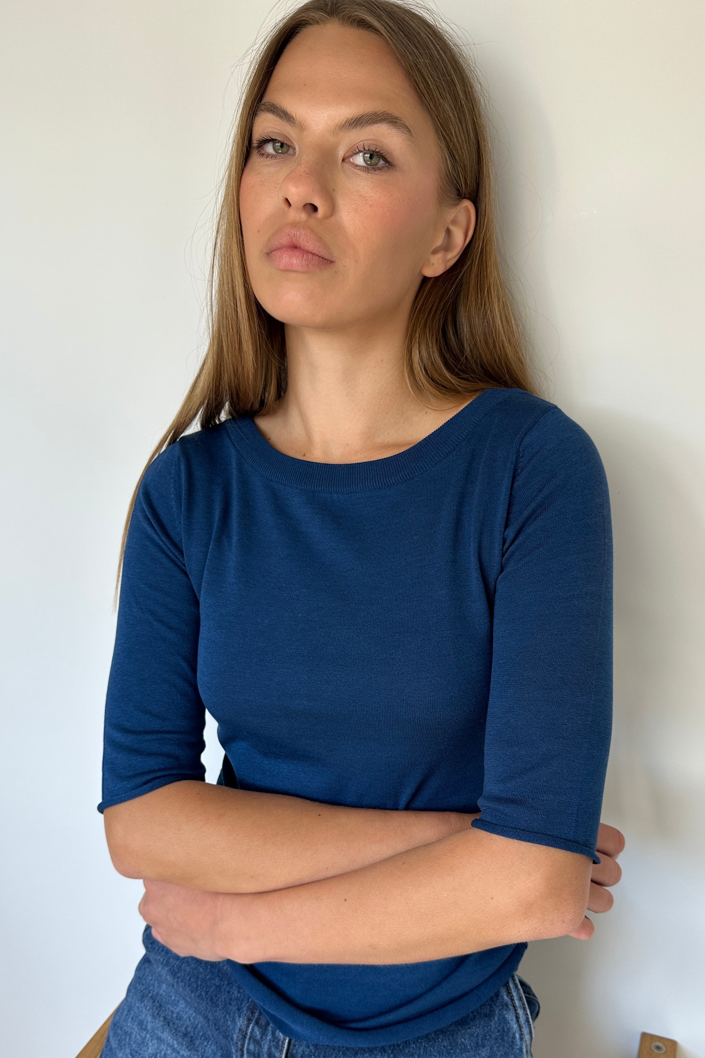Woman wearing a blue top and jeans against a white wall