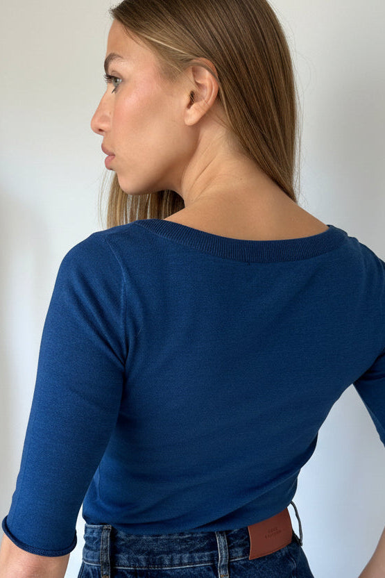 Person wearing a blue top back view, and jeans against a plain background