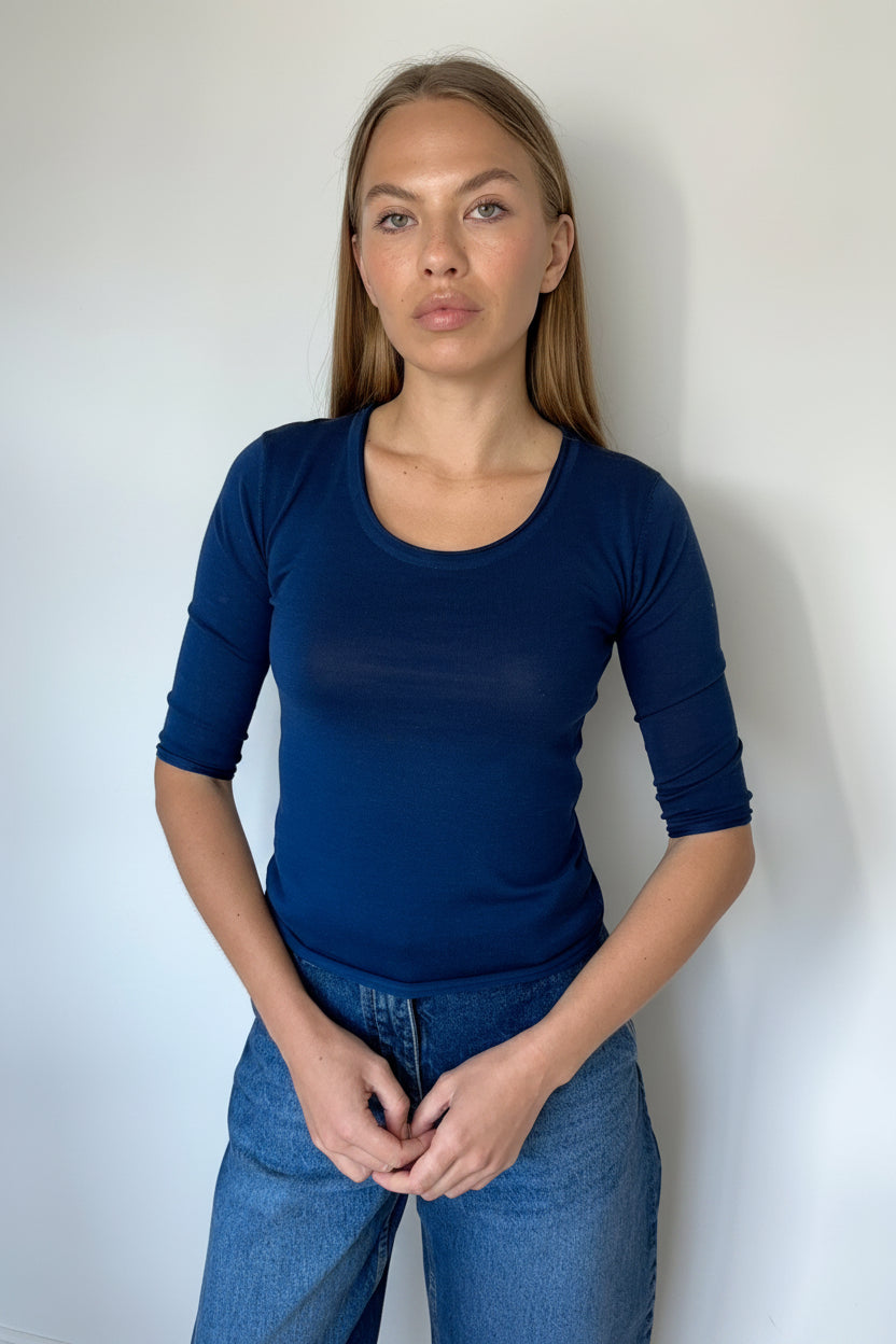 Woman wearing a blue top and jeans against a plain background
