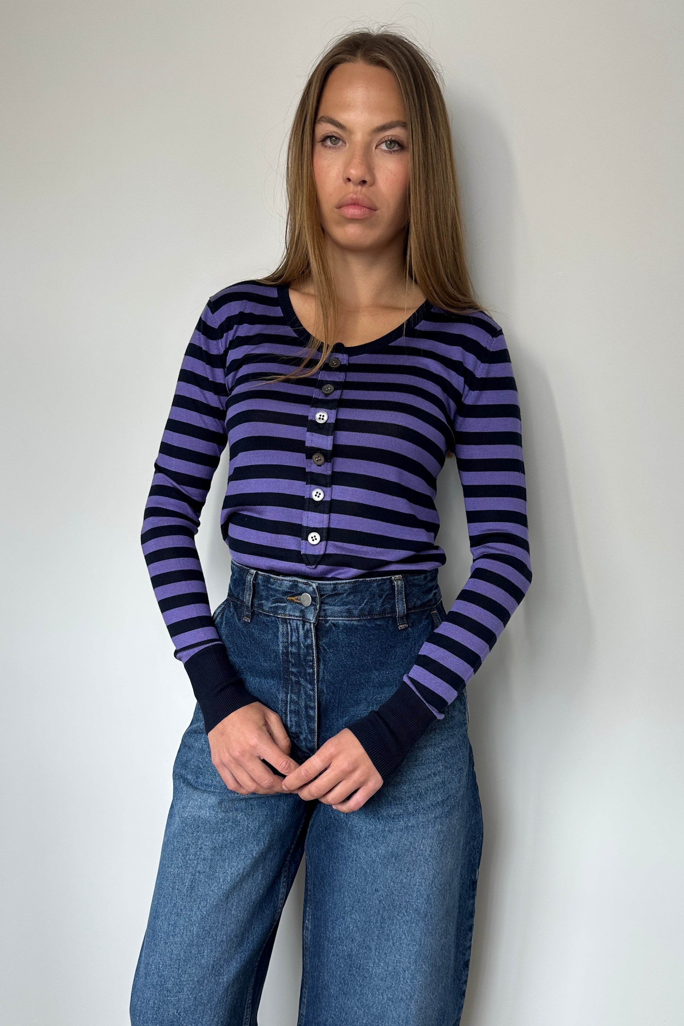 Woman wearing a striped shirt and jeans against a plain background