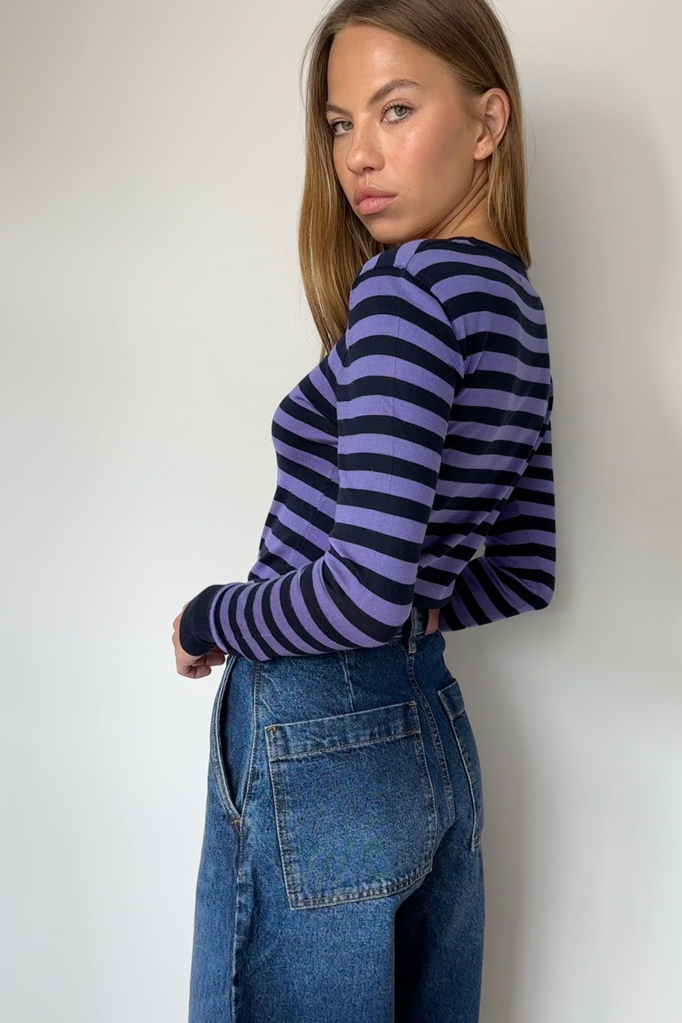 Person wearing a striped sweater and jeans against a white wall