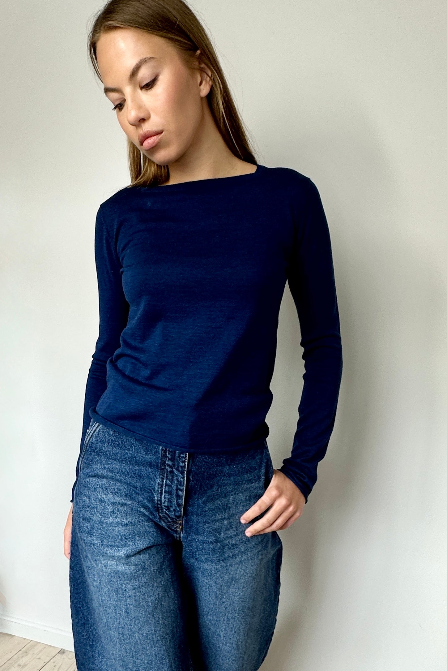 Woman wearing a navy blue sweater and jeans against a plain background