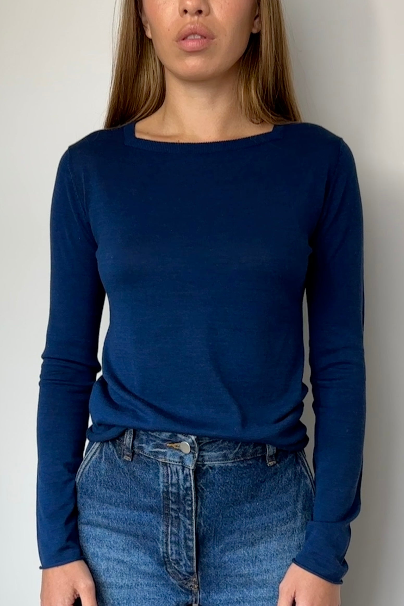 Person wearing a blue long-sleeve top and jeans against a plain background