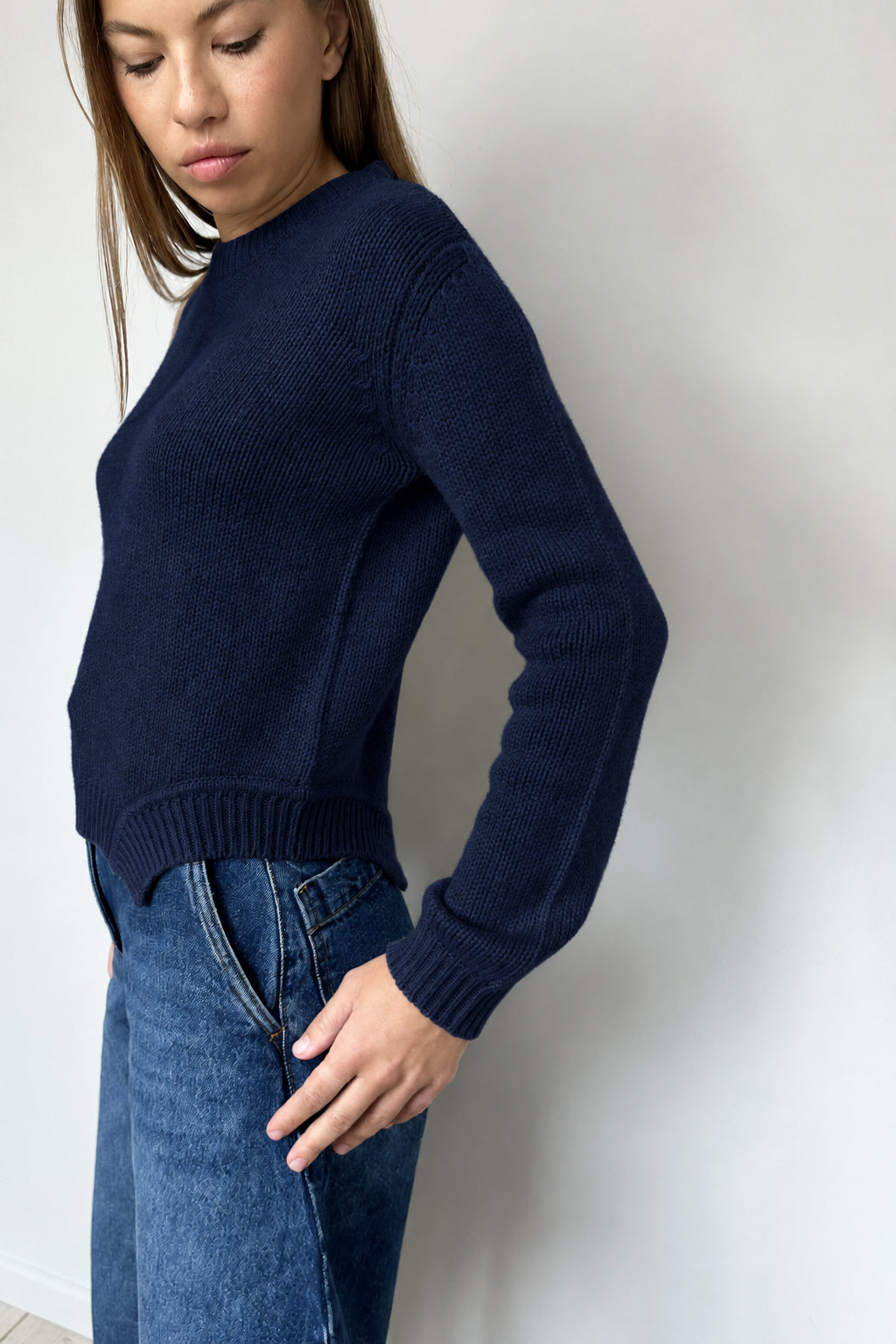 Woman wearing navy sweater and blue jeans against a plain background