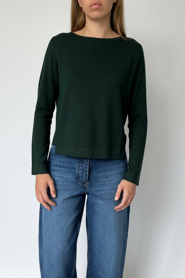 Person wearing a dark green sweater and blue jeans standing on a white floor.