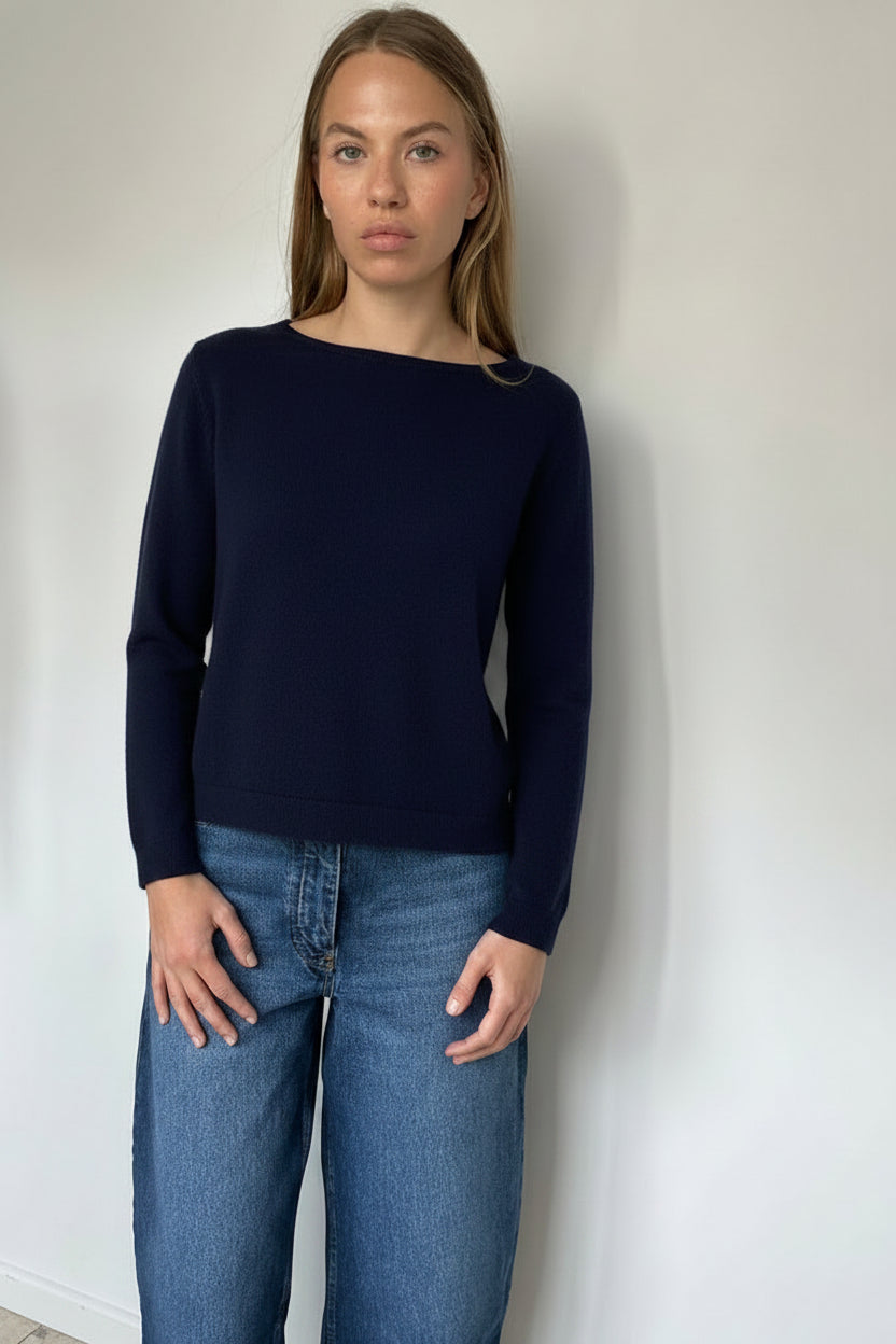 Person wearing a navy sweater and blue jeans against a white wall.