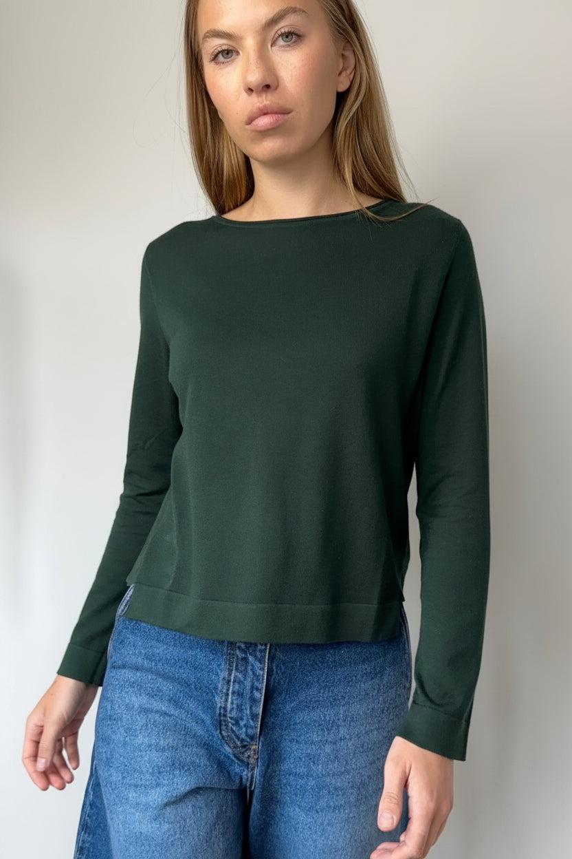 Woman wearing a green sweater and blue jeans against a plain background