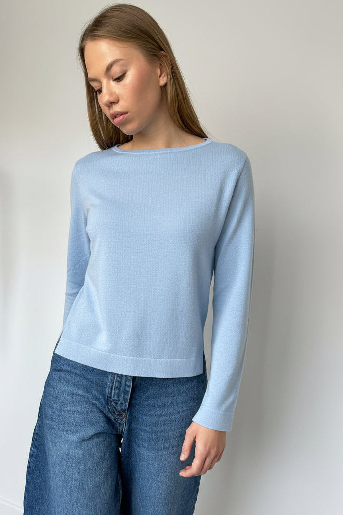 Woman wearing a dark green sweater and blue jeans against a plain background