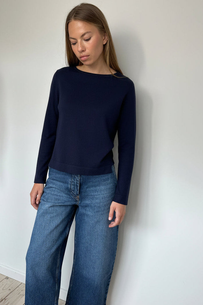 Woman wearing a navy sweater and blue jeans against a white wall
