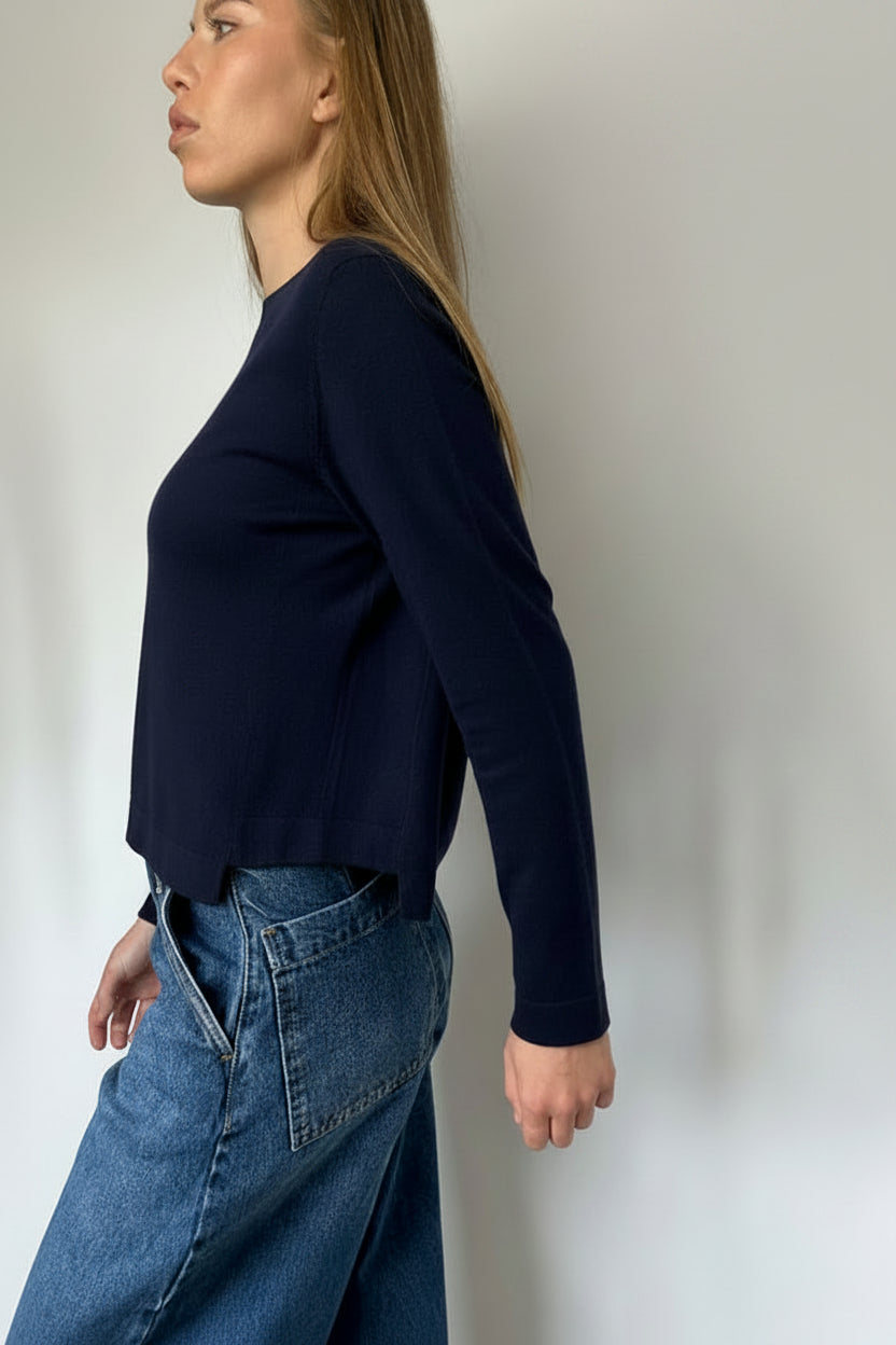 Person wearing a navy blue sweater and blue jeans against a plain background