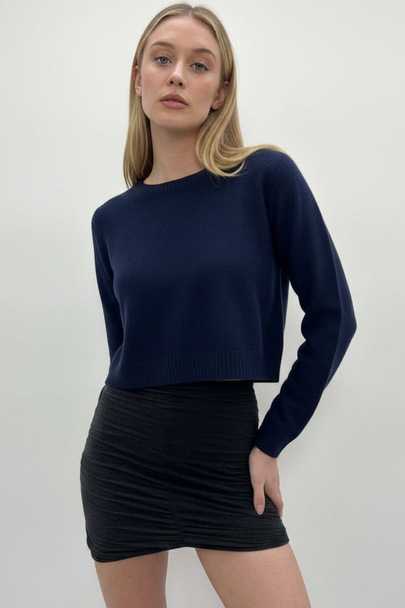 Woman wearing a navy blue sweater and black skirt against a plain background