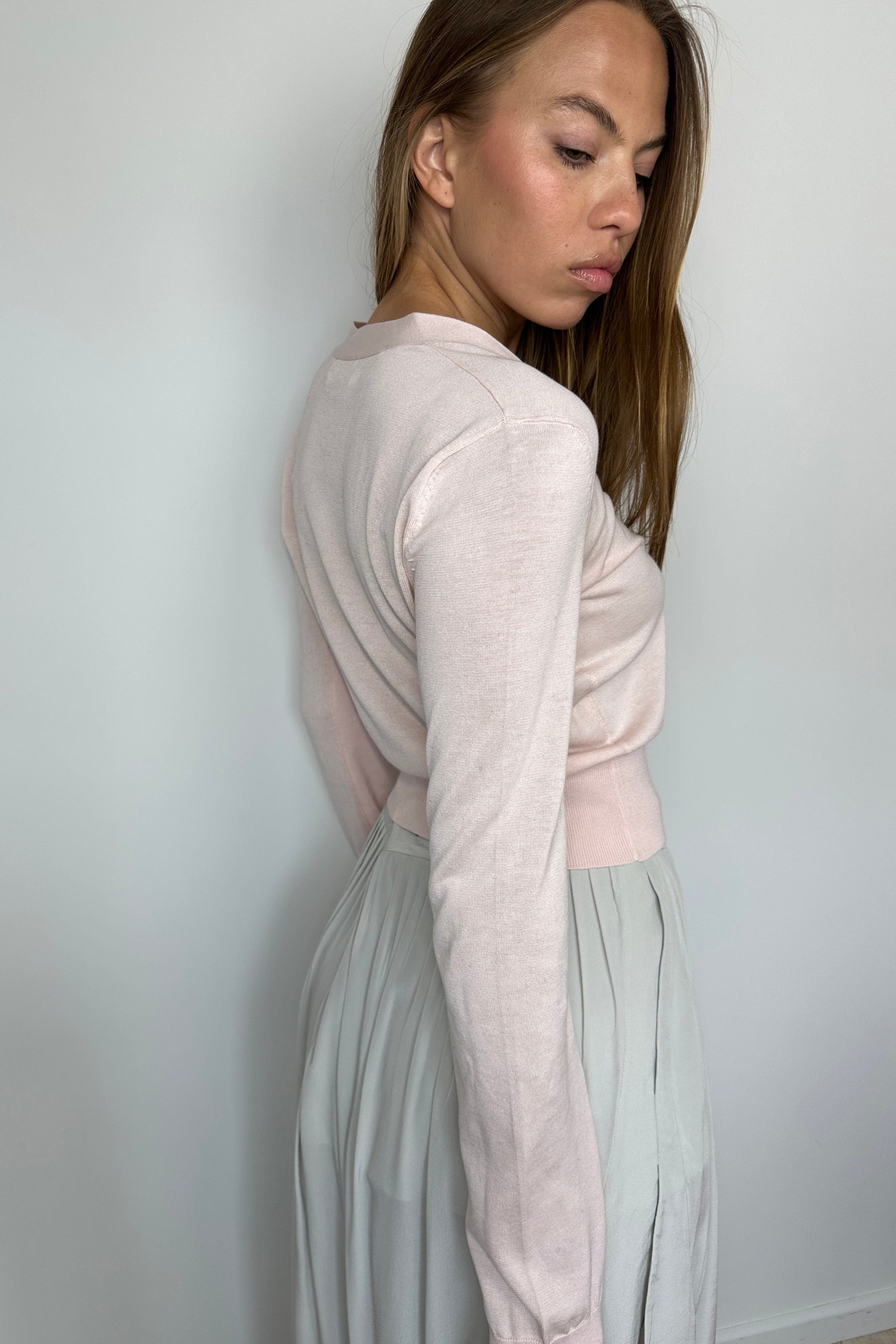 Woman, side view, wearing a light pink top and gray skirt.