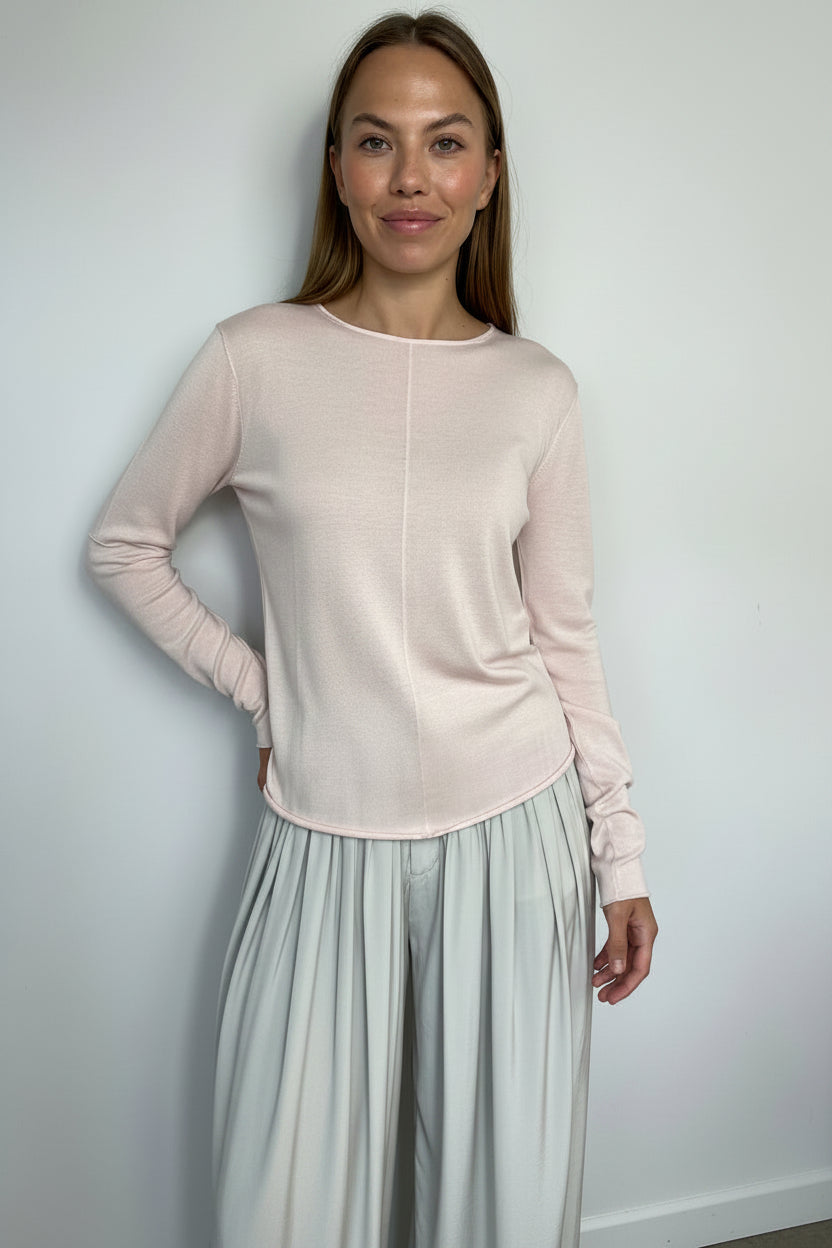 Woman wearing a light pink long-sleeve top and light gray pleated pants against a white background