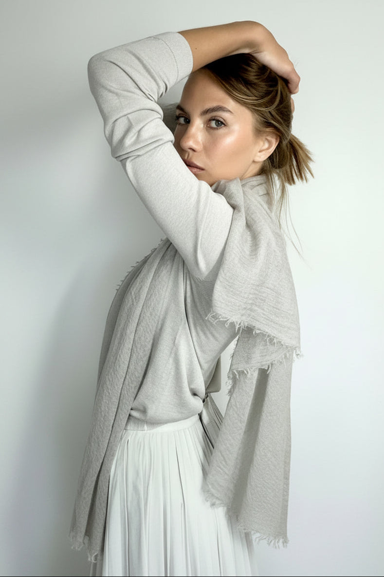 Woman wearing a light gray scarf and sweater and white skirt against a plain background