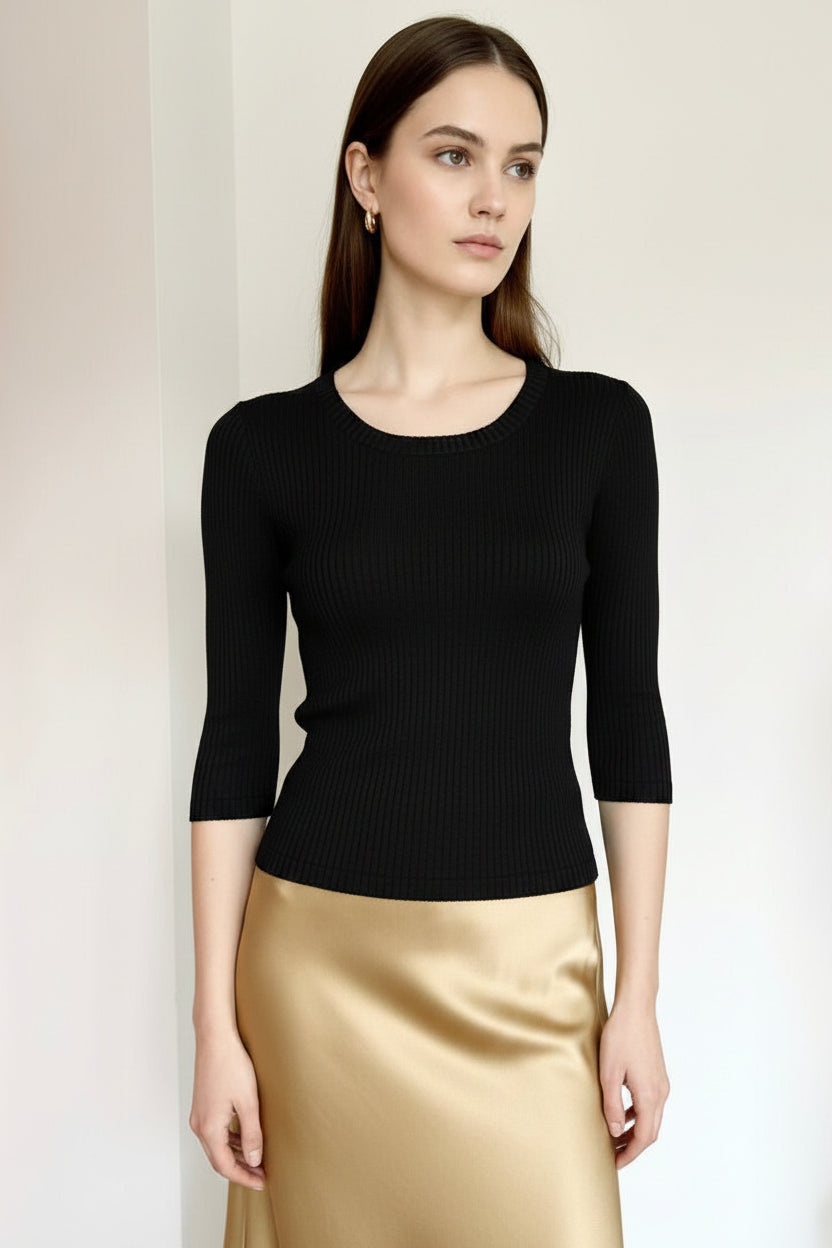 Woman wearing a black top and gold skirt against a plain background