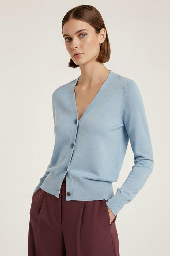 Woman wearing a light blue cardigan and brown pants on a plain background