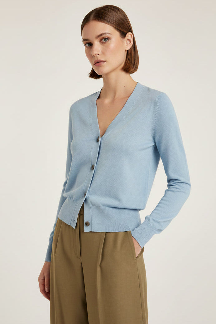 Woman wearing a light blue cardigan and brown pants on a plain background