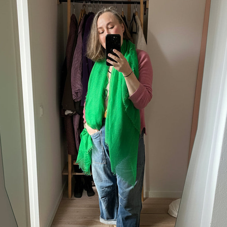 Person wearing a green scarf and blue jeans standing in front of a mirror.