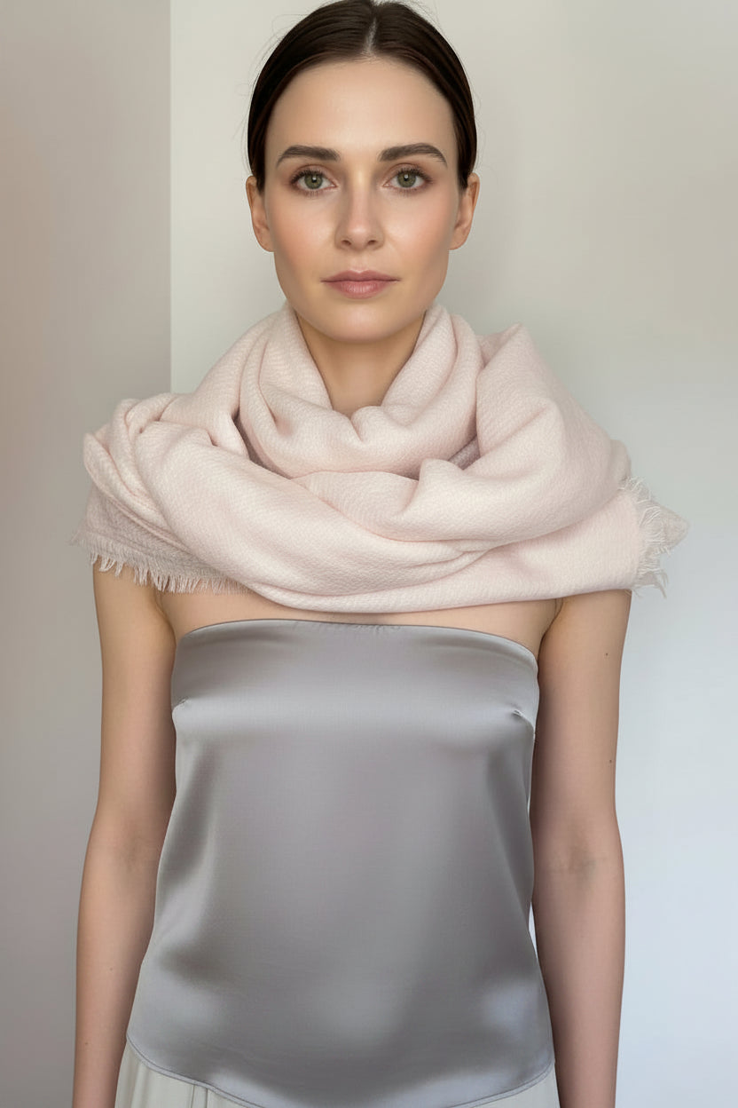Woman wearing a light pink scarf and light gray outfit against a plain background