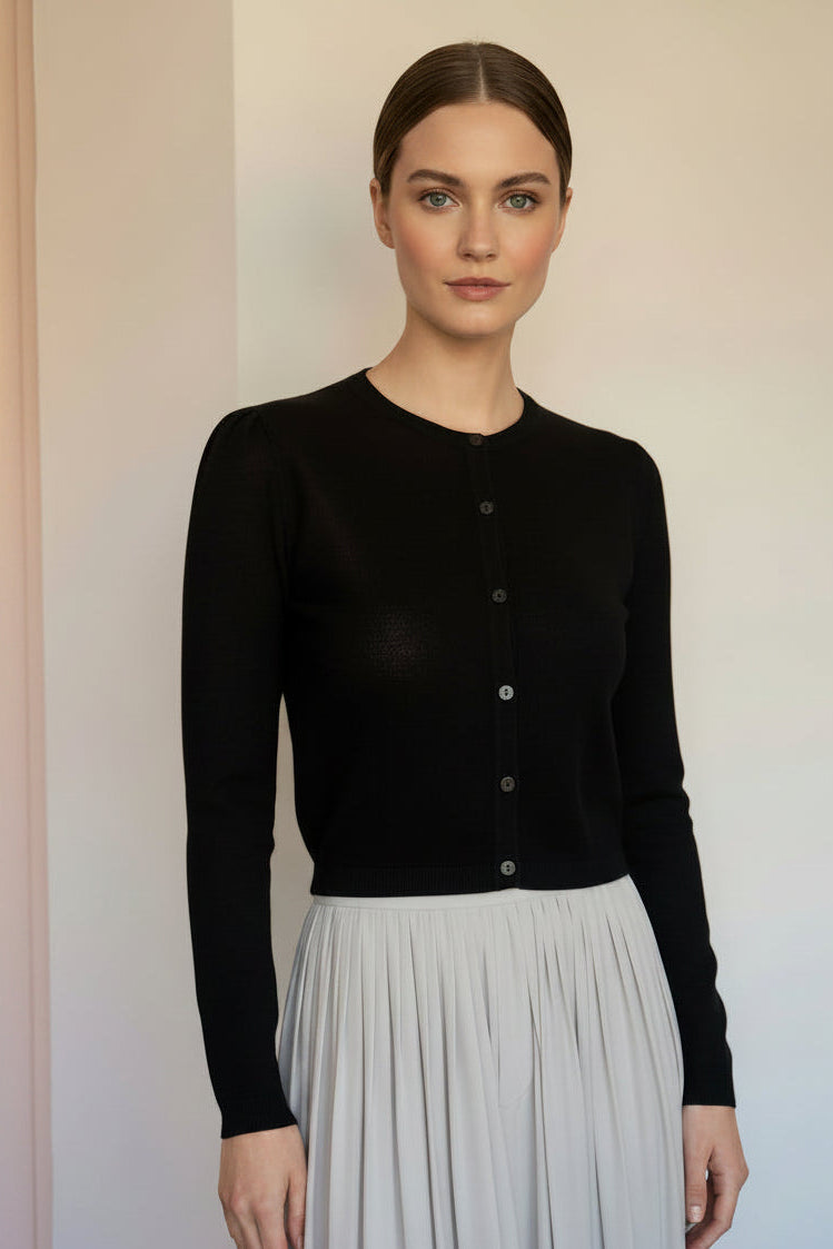 A black long-sleeve knit cardigan with a button-up front, on a model, paired with a light gray pleated skirt.