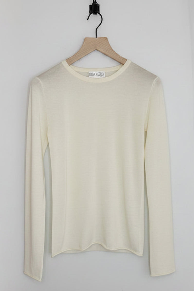 A cream-colored long-sleeve knit top hanging on a wooden hanger against a plain light gray wall.