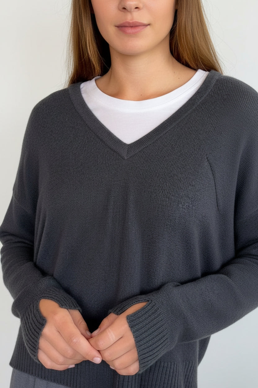 A woman wearing a dark charcoal gray v-neck knit sweater and matching gray skirt, standing against a plain light gray wall.
