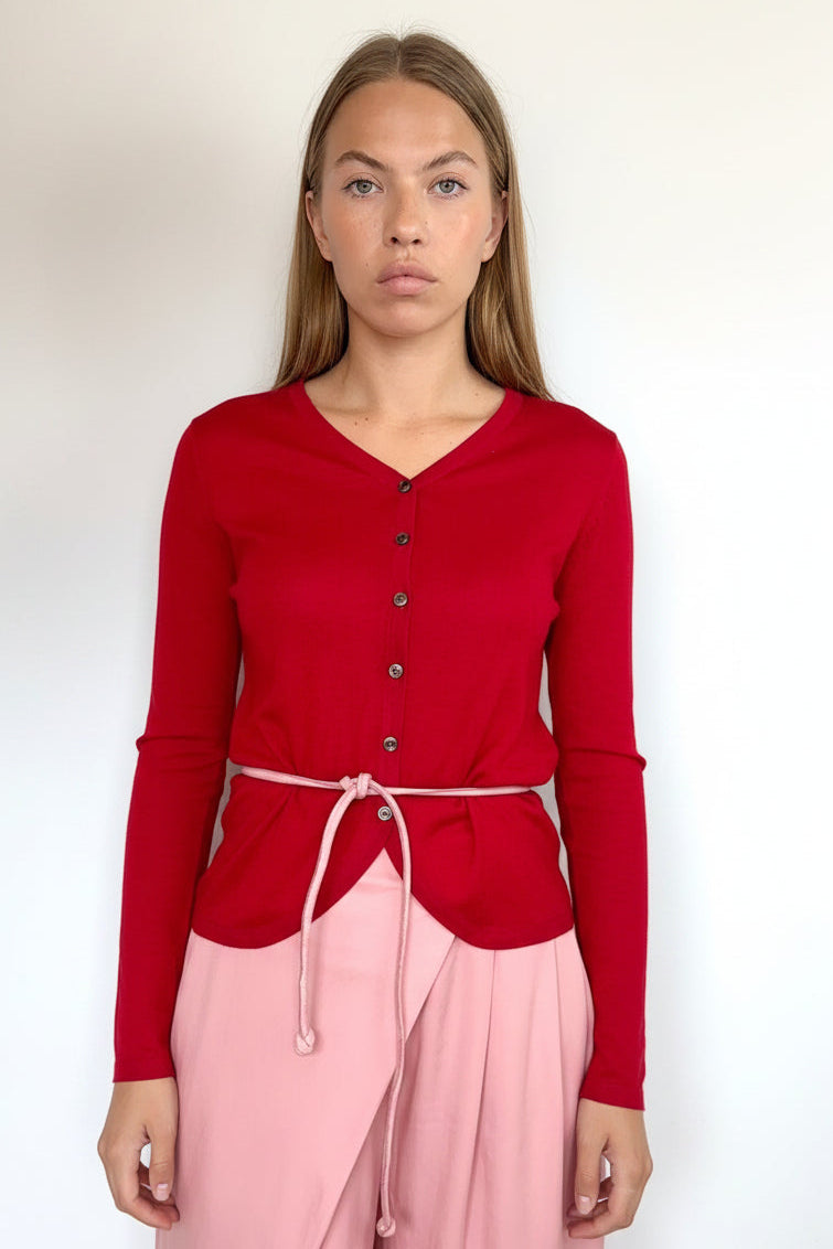 A woman modeling a red long-sleeve button-front top with a drawstring waist tie, paired with light pink wrap-style pants, against a plain white background.
