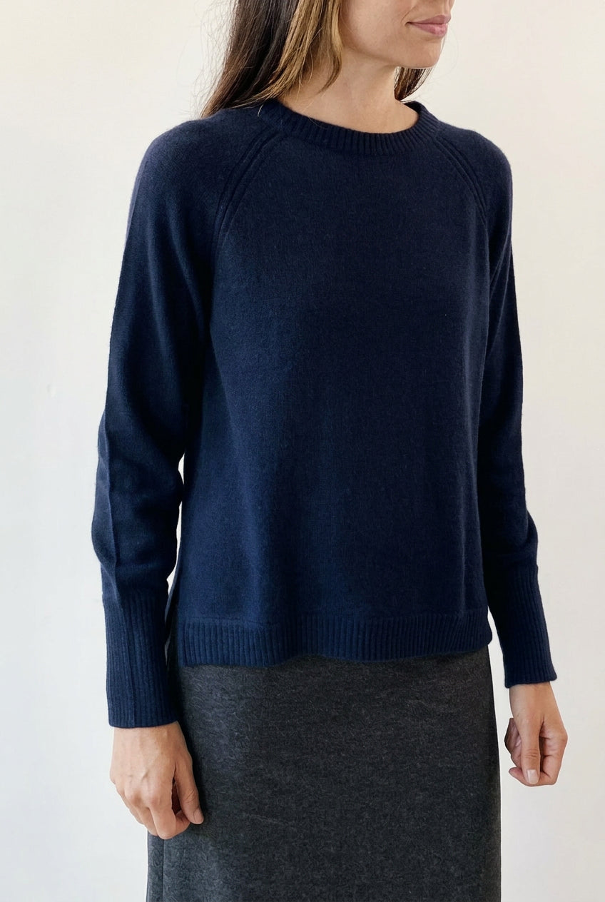 Person wearing a dark blue sweater and gray skirt on a plain background